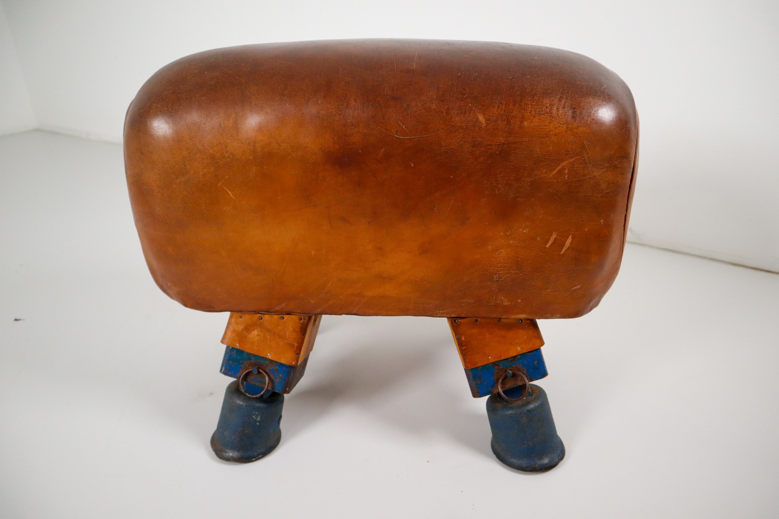 Strong, vintage European gymnasium bench with a patinated leather covered top that sits in to the bench's solid wooden frame. The gym bench frame maintains its original markings where the straps and r Early-20th century