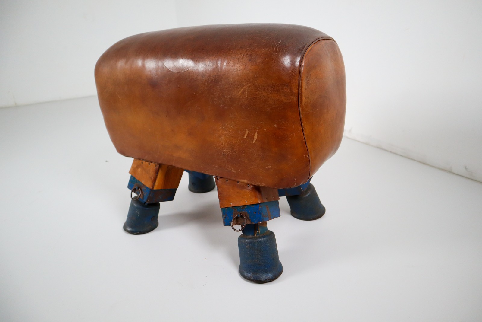 Strong, vintage European gymnasium bench with a patinated leather covered top that sits in to the bench's solid wooden frame. The gym bench frame maintains its original markings where the straps and r Early-20th century