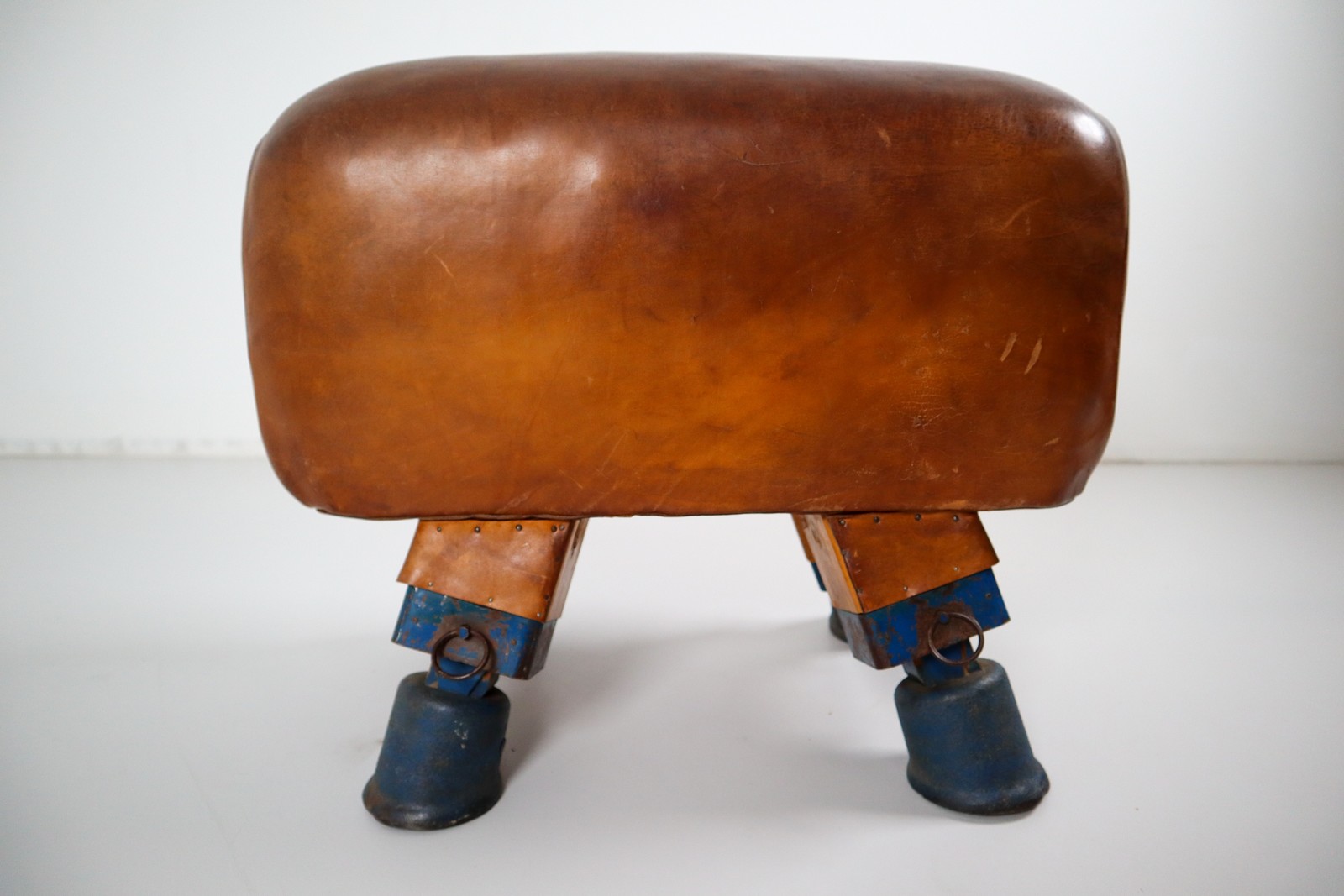 Strong, vintage European gymnasium bench with a patinated leather covered top that sits in to the bench's solid wooden frame. The gym bench frame maintains its original markings where the straps and r Early-20th century