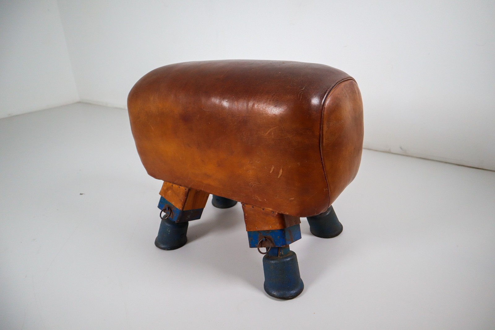 Strong, vintage European gymnasium bench with a patinated leather covered top that sits in to the bench's solid wooden frame. The gym bench frame maintains its original markings where the straps and r Early-20th century