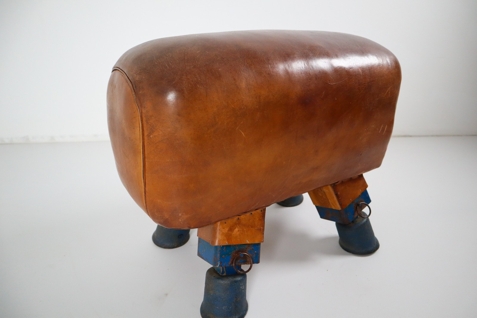 Strong, vintage European gymnasium bench with a patinated leather covered top that sits in to the bench's solid wooden frame. The gym bench frame maintains its original markings where the straps and r Early-20th century