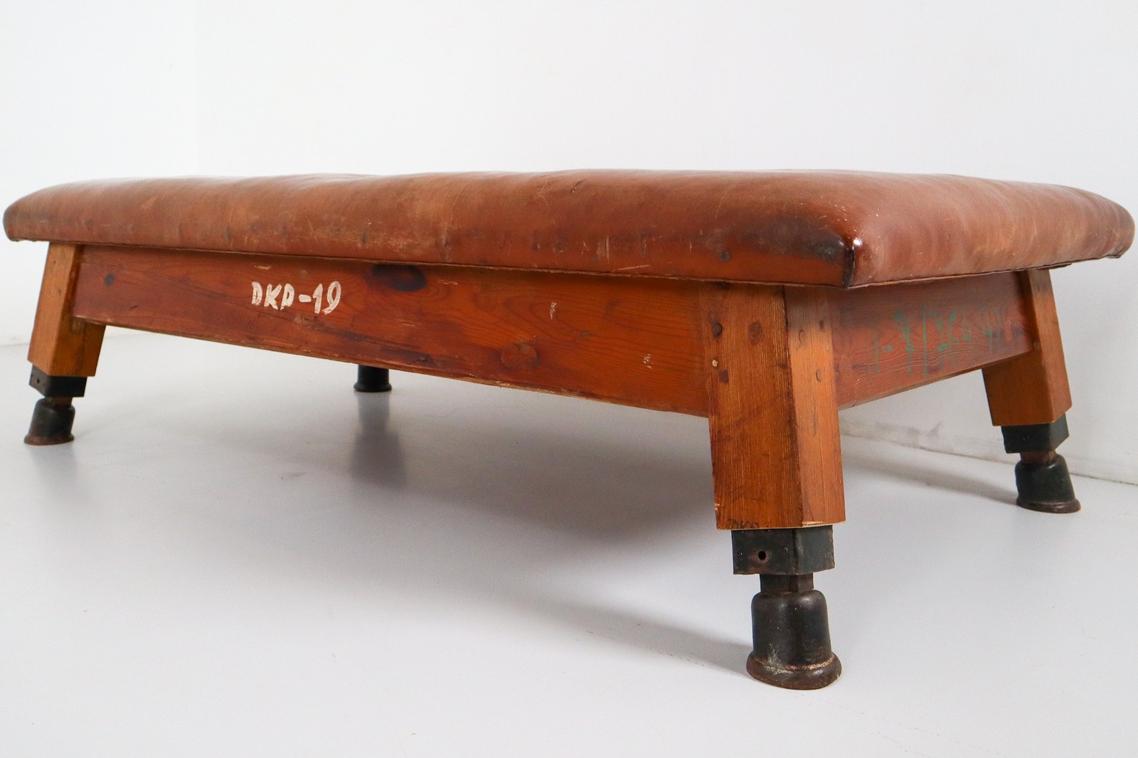 Strong, vintage European gymnasium bench with a patinated leather covered top that sits in to the bench's solid wooden frame. The gym bench frame maintains its original markings where the straps and r Mid-20th century